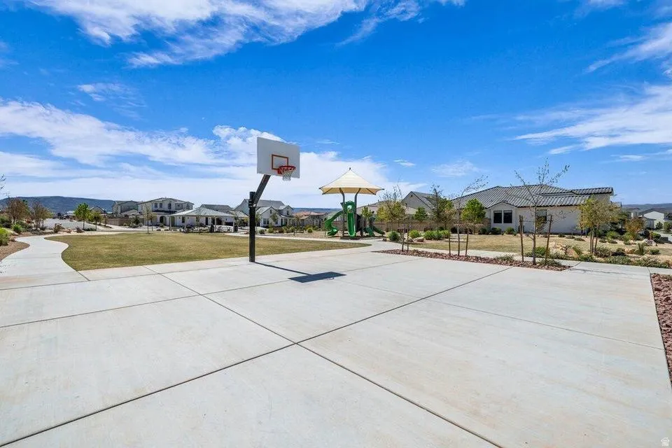 Expansive concrete court featuring a regulation basketball hoop, mature landscaping, and open sightlines