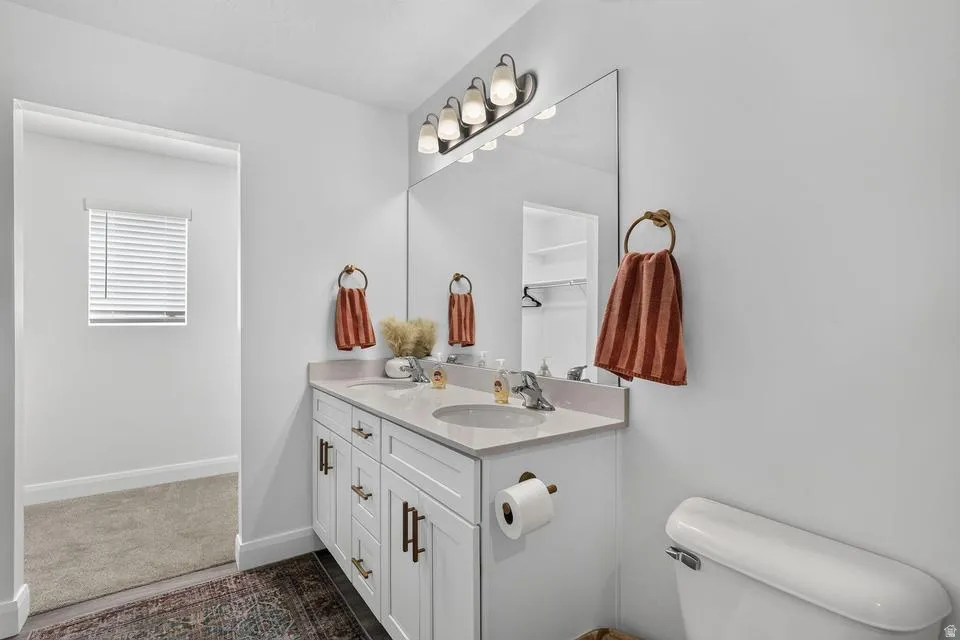 Dual sink vanity featuring white cabinetry, bronze hardware, a light-toned countertop, and a large mirror