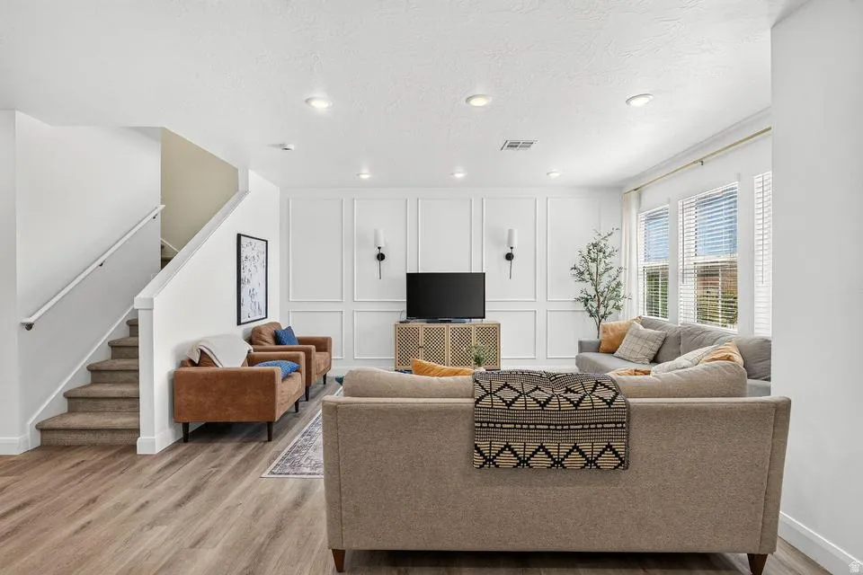 Spacious living area featuring wood-finish flooring, recessed lighting, and a decorative paneled accent wall with sconce lighting