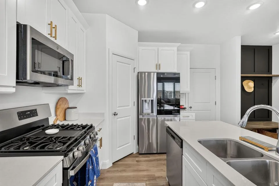 Modern kitchen featuring white cabinetry with brass hardware, stainless steel appliances including a gas cooktop and French-door refrigerator, dual stainless steel sinks with undermount installation, white quartz countertops, recessed ceiling lighting, an