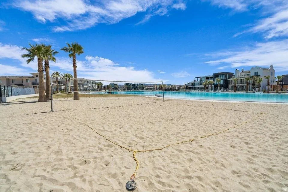 Sandy beach volleyball court with a net, bordered by palm trees and a large artificial lagoon