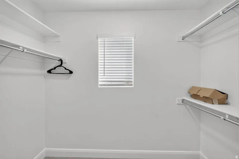 Walk-in closet with white shelving, chrome hanging rods, and a window with horizontal blinds
