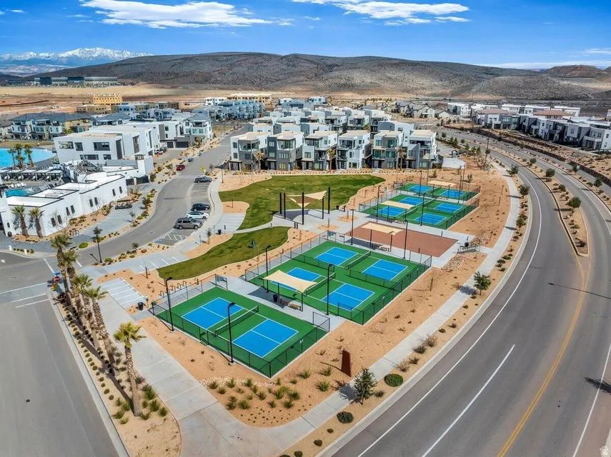 Modern residential community featuring resort-style amenities including multiple pickleball courts with professional-grade playing surfaces, manicured green space with mature landscaping, and contemporary white architectural homes