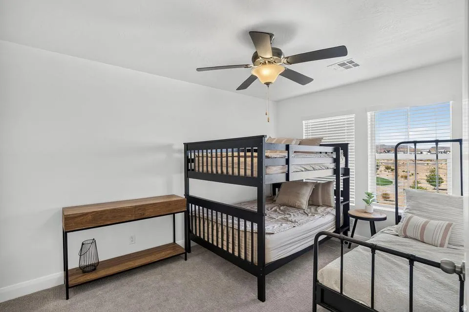 Carpeted room featuring white walls, dual windows with horizontal blinds, and a built-in ceiling fan with integrated lighting