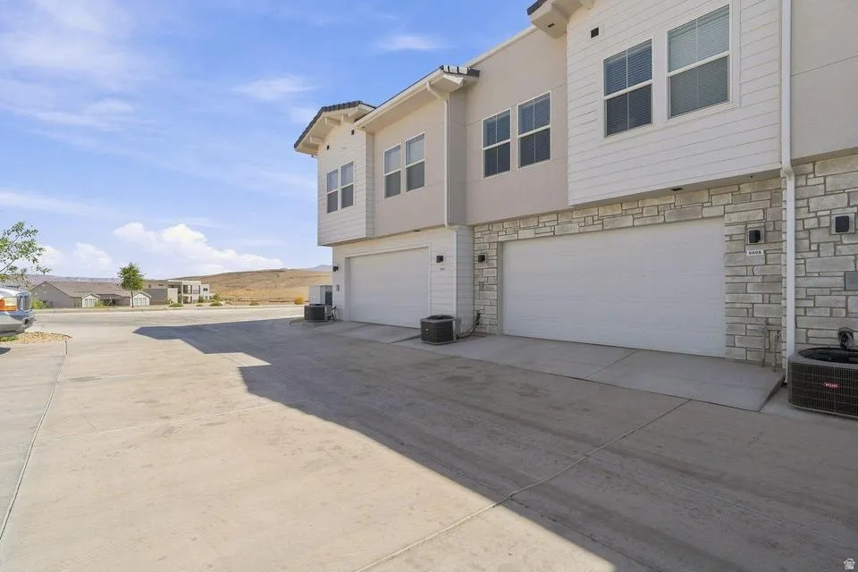 Spacious driveway with expansive concrete apron featuring two-car garage with white panel doors