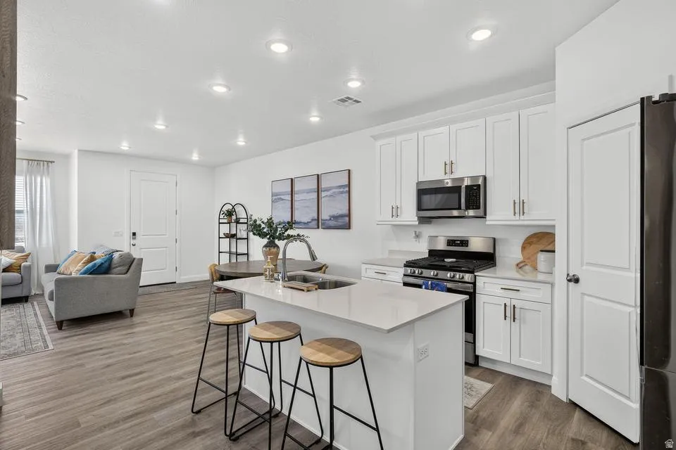 Open-concept kitchen featuring white shaker cabinetry, stainless steel appliances, a white subway tile backsplash, and a central island with a solid surface countertop