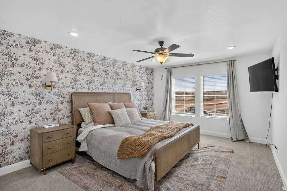 Spacious primary bedroom featuring a wood-frame sleigh bed, wood-finish nightstand, ceiling fan with integrated lighting, recessed ceiling lights, and large glass doors opening to a balcony with exterior views