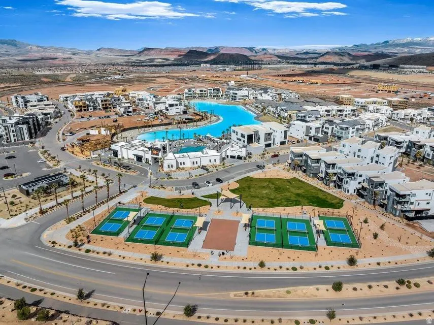 Aerial view of a resort-style community featuring a striking lagoon-shaped saltwater pool with lounging areas, professional-grade tennis courts, manicured landscaping with native desert plantings, and contemporary white residential architecture throughout