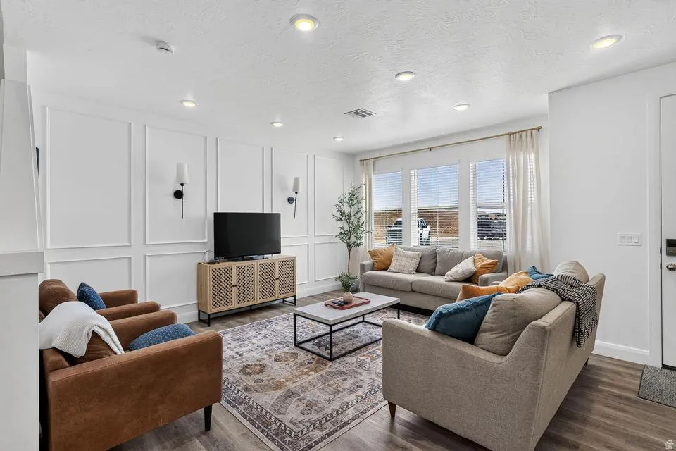 Sophisticated living room showcasing recessed ceiling lighting, white shaker-style wall paneling, and wide windows with natural light