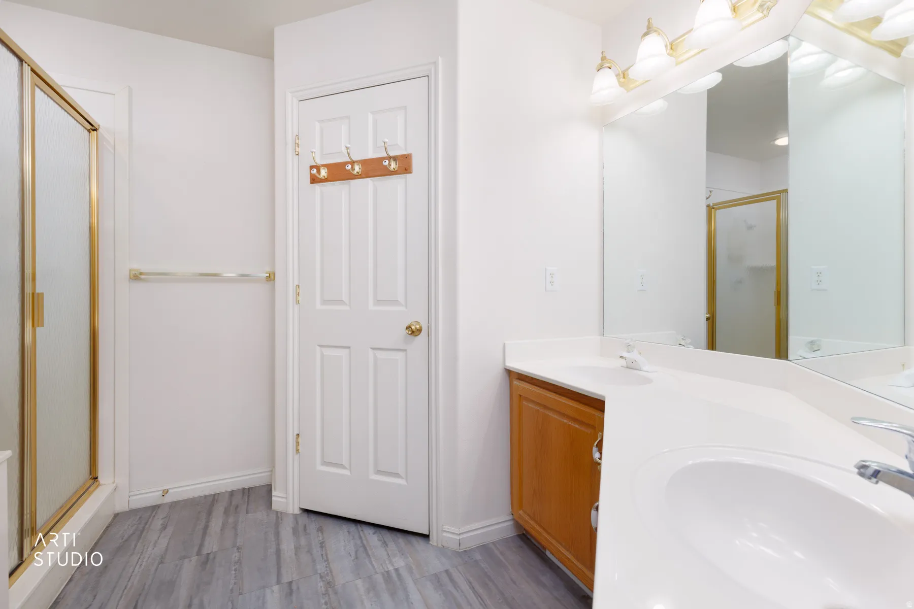 Spa-inspired primary bathroom featuring dual vanities with wood-finish cabinetry, white quartz countertops, and polished brass hardware
