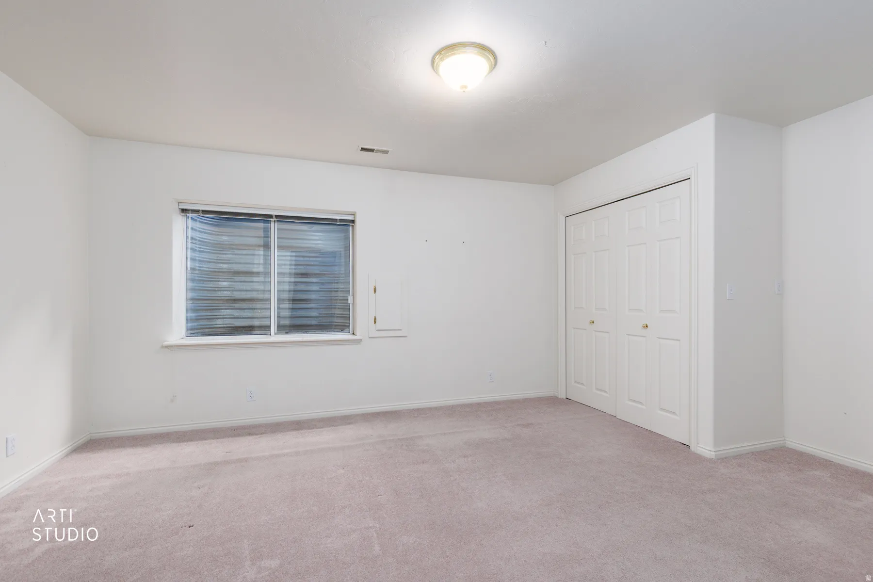 Neutral-toned room featuring a window with horizontal blinds, a flush-mount ceiling light fixture, and a spacious bi-fold closet