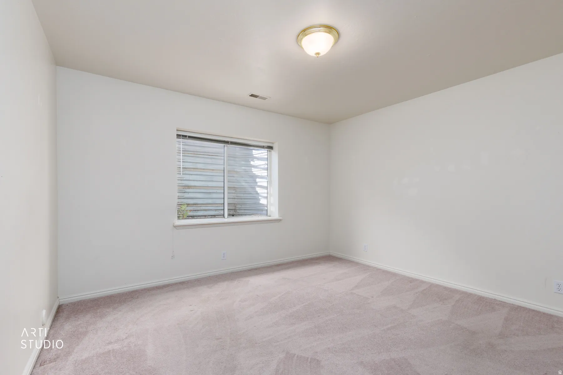 Bright bedroom with neutral carpeting, recessed ceiling lighting, and a horizontal slider window with blinds providing natural light and privacy control
