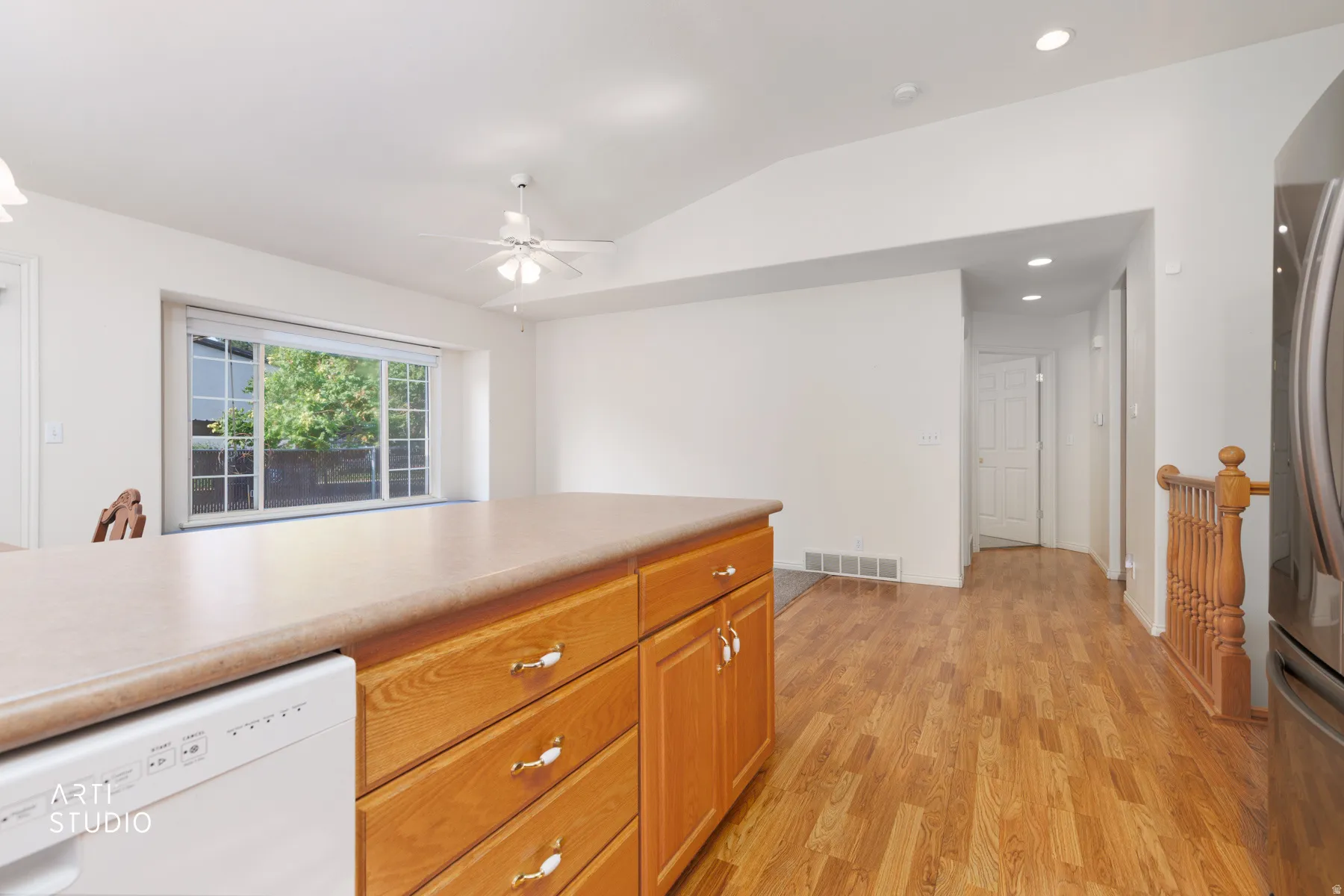 Spacious kitchen featuring warm wood-finish cabinetry with multiple drawers and storage, white countertops, stainless steel appliances, and wood-finish flooring throughout