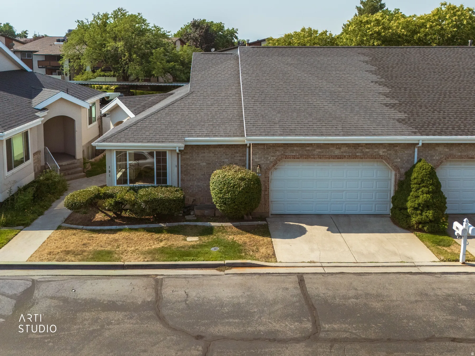 Brick ranch home featuring a two-car garage with light blue panel doors, a manicured front landscape with established shrubs and boxwoods, a concrete driveway, and a composite asphalt shingle roof