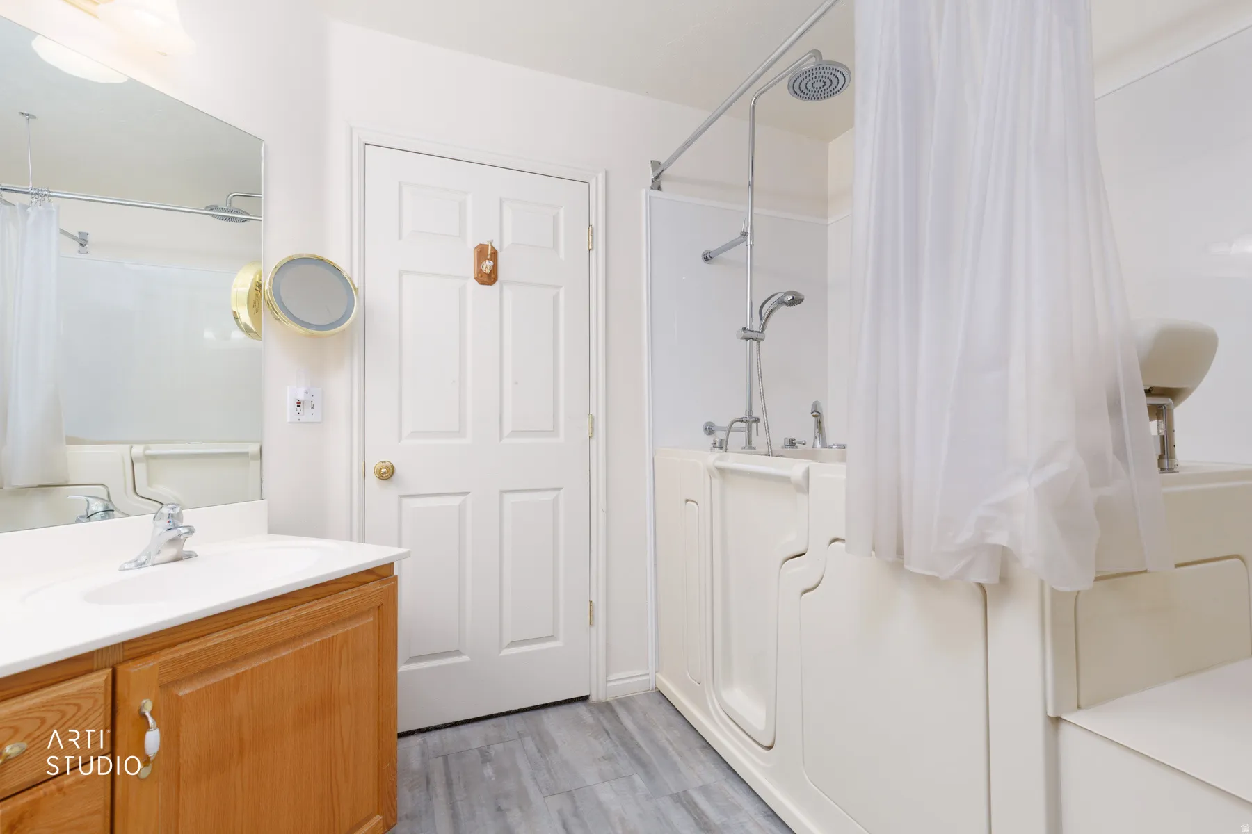 Bathroom featuring a walk-in tub with shower, single vanity with wood-finish cabinetry, and light gray wood-finish flooring