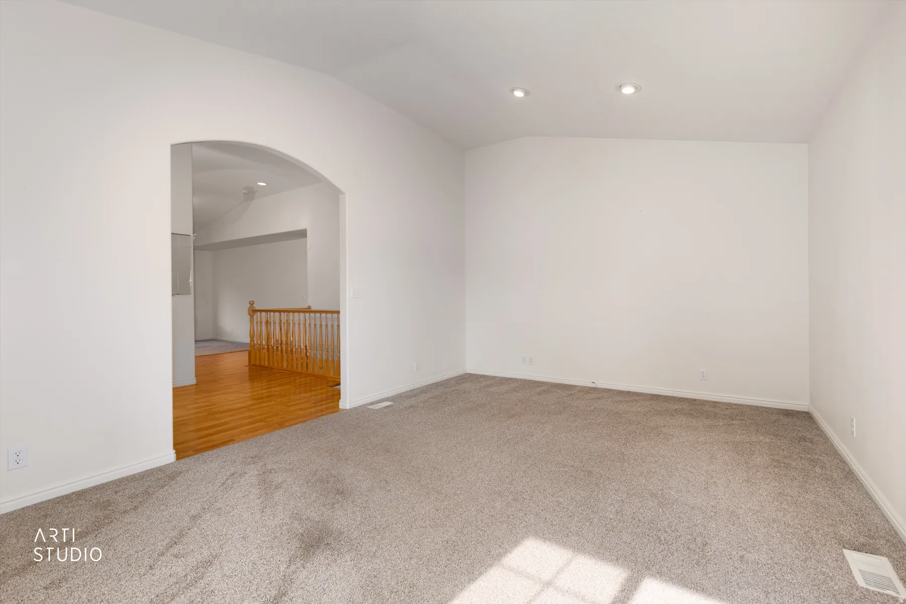 Spacious carpeted room with recessed ceiling lighting and an arched doorway leading to a hardwood-floored secondary space