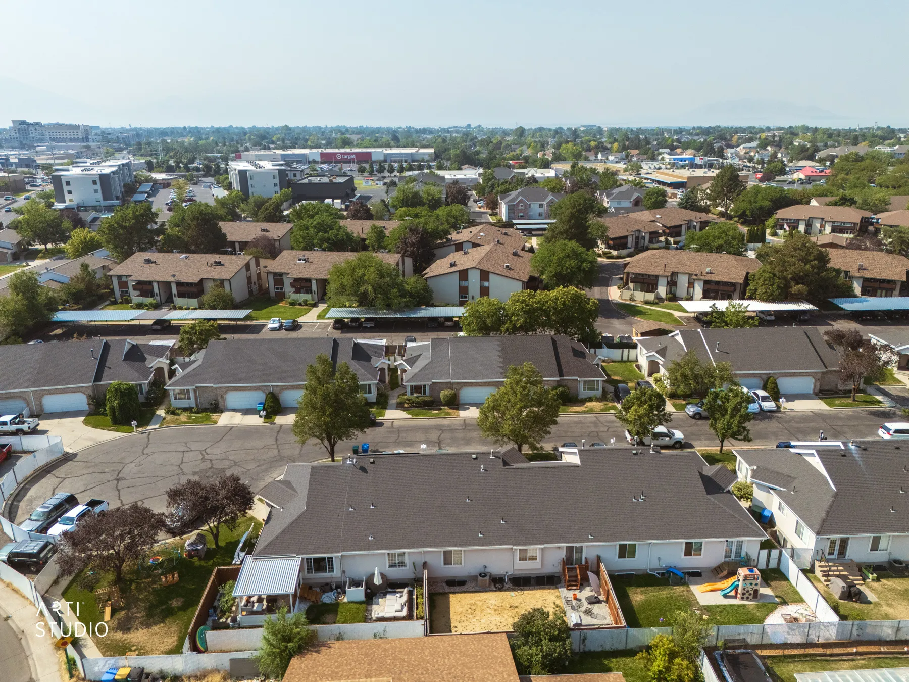 Aerial view showcasing a contemporary residential community featuring low-profile architectural design with flat rooflines, integrated landscaping with mature trees throughout the neighborhood, and organized street-level parking