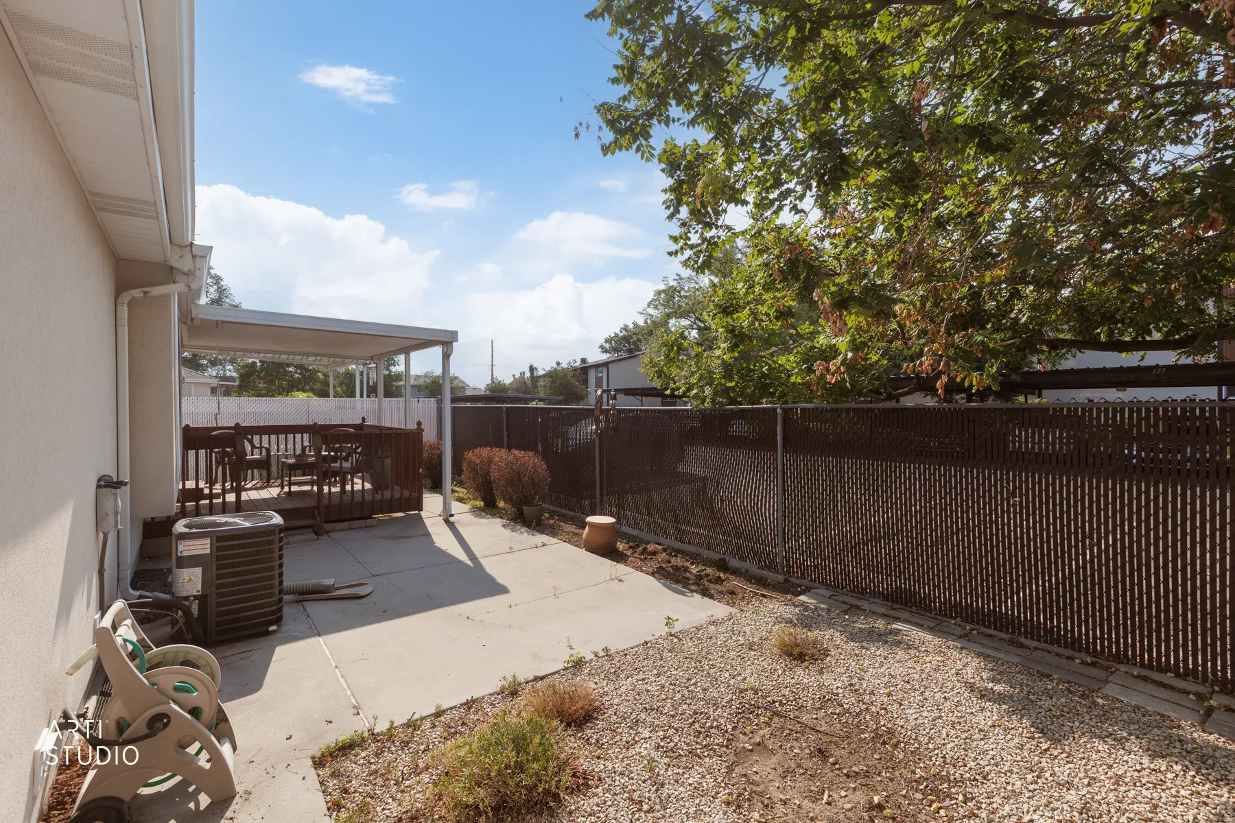Outdoor patio area featuring a covered deck with wood-finish railing, concrete slab, and a gravel-covered section