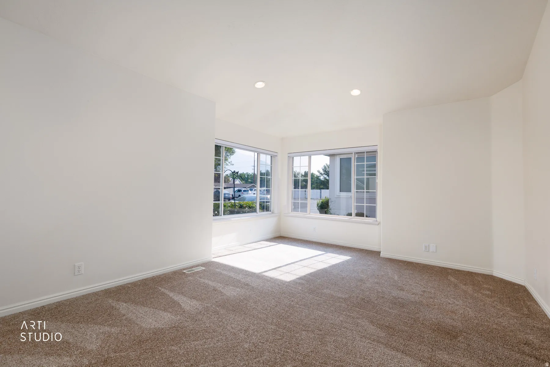 Spacious room featuring neutral carpeting, white walls, recessed lighting, and multiple windows with white frames