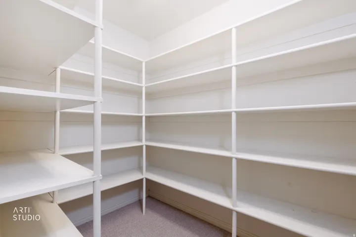 Spacious walk-in closet featuring extensive white shelving spanning multiple walls, offering abundant storage