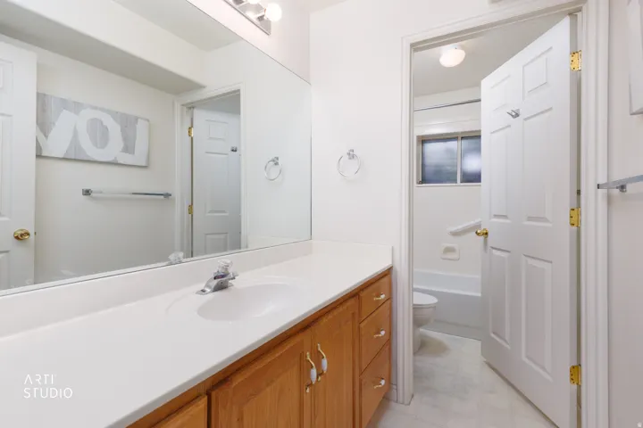 Spacious primary bathroom featuring a wood-finish vanity with dual handles, white quartz countertop, and an undermount sink