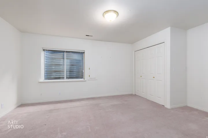 Neutral-toned room featuring a window with horizontal blinds, a flush-mount ceiling light fixture, and a spacious bi-fold closet
