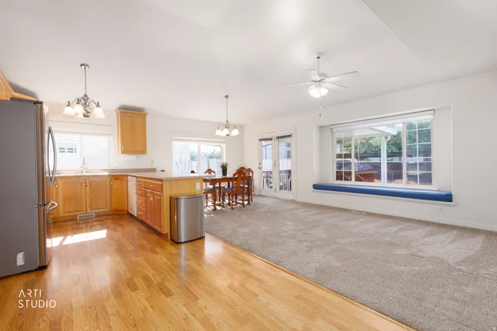 Open-concept living space featuring warm wood-finish flooring, custom wood cabinetry with stainless steel appliances, and abundant natural light from multiple large windows