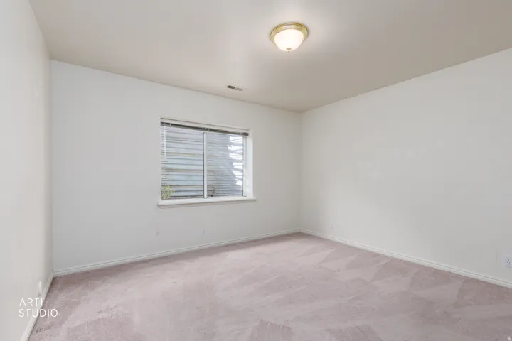 Bright bedroom with neutral carpeting, recessed ceiling lighting, and a horizontal slider window with blinds providing natural light and privacy control