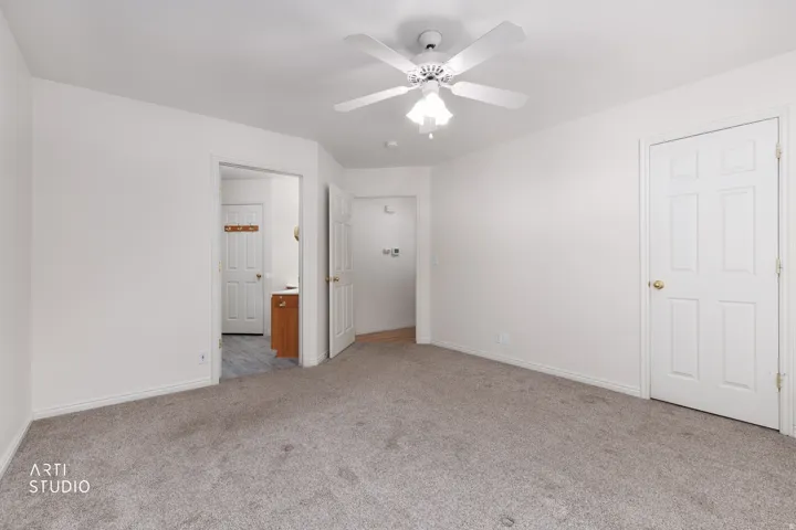 Spacious primary bedroom featuring neutral carpet flooring, ceiling fan with integrated lighting, and dual closet access
