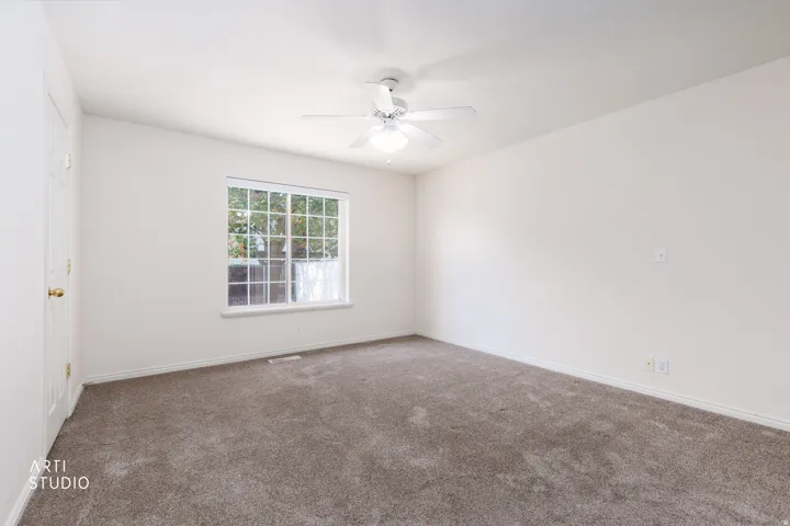 Spacious bedroom featuring neutral carpeting, ceiling fan with integrated lighting, and a large multi-pane window allowing abundant natural light