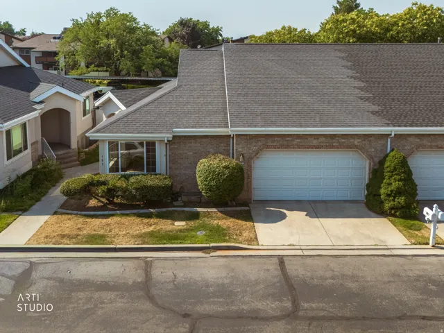 Brick ranch home featuring a two-car garage with light blue panel doors, a manicured front landscape with established shrubs and boxwoods, a concrete driveway, and a composite asphalt shingle roof