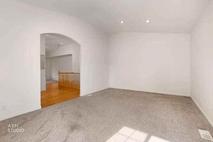 Spacious carpeted room with recessed ceiling lighting and an arched doorway leading to a hardwood-floored secondary space