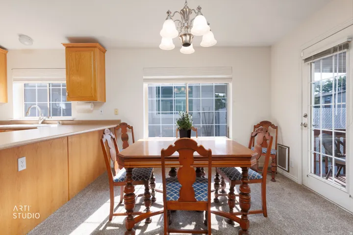 Bright dining area featuring a round wood pedestal table, coordinating wood chairs with upholstered seats, and abundant natural light from multiple large windows