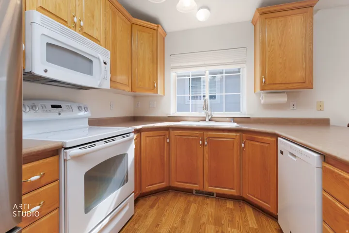 Efficient kitchen layout featuring warm wood cabinetry, white appliances including a microwave and electric range, laminate countertops, and wood-finish flooring