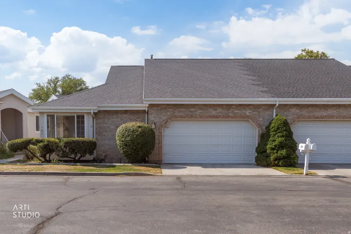 Brick ranch-style residence featuring a two-car attached garage with decorative arched detailing, manicured landscaping with established shrubs and evergreen plantings, and a clean asphalt driveway