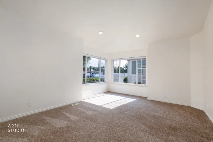 Spacious room featuring neutral carpeting, white walls, recessed lighting, and multiple windows with white frames