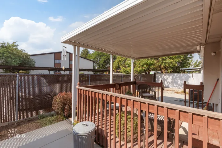 Covered patio with white aluminum louvered roof system, warm wood-finish railing, and concrete flooring