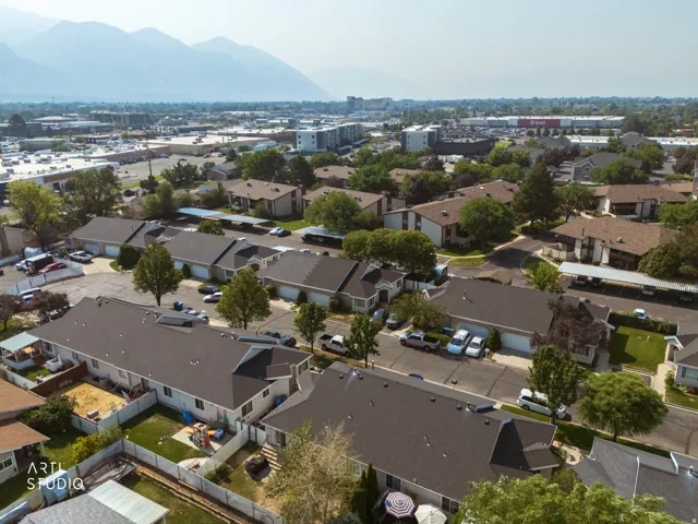 Aerial view of a residential neighborhood featuring single-story homes with dark composite roofing, mature landscaping with established trees throughout the properties, and paved driveways