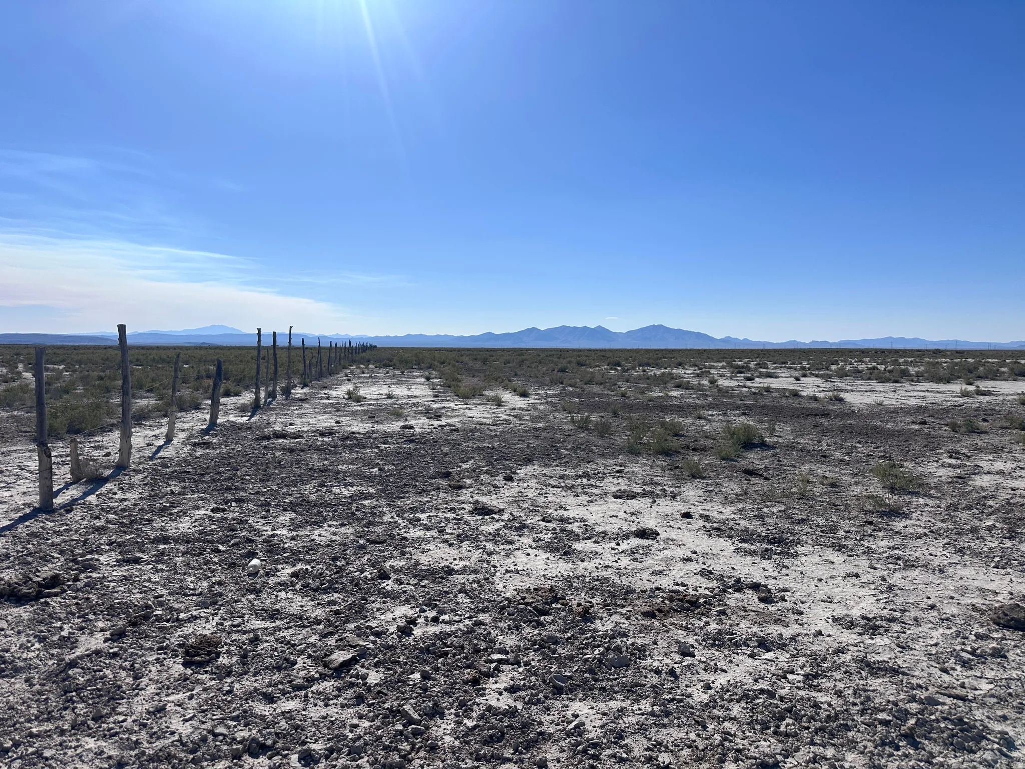Expansive desert landscape featuring a clear sky, distant mountain range, natural vegetation, and a rustic wooden fence line