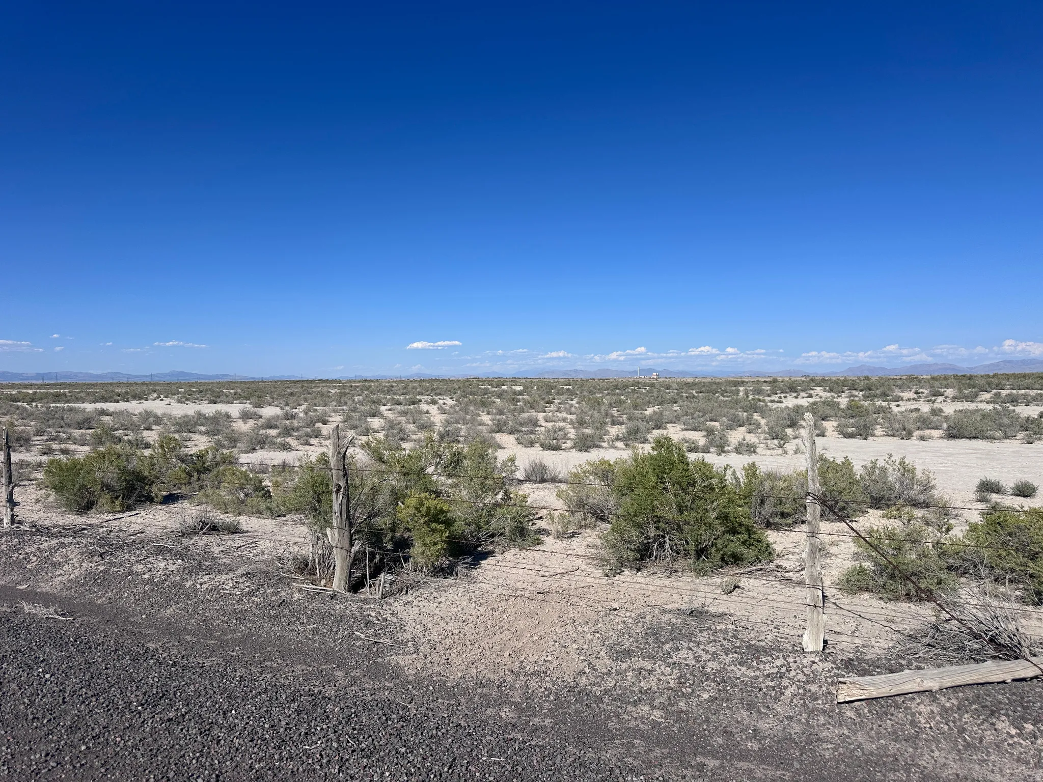 Expansive desert landscape featuring natural scrub brush and distant mountain ranges under a clear blue sky