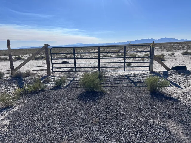 Gated ranch entrance featuring a sturdy metal cattle gate with horizontal bar design, set on a gravel base