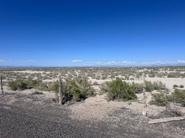 Expansive desert landscape featuring natural scrub brush and distant mountain ranges under a clear blue sky