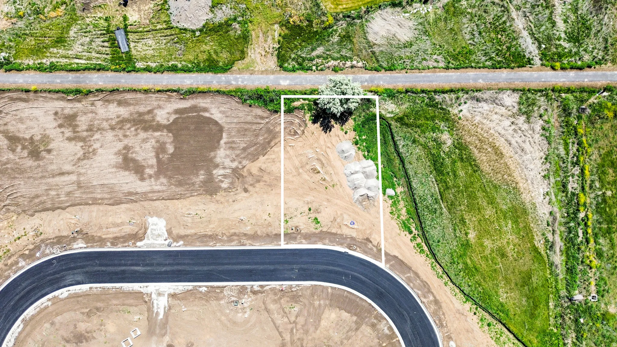 Aerial view of a vacant lot outlined in white, featuring a paved road at the foreground and a secondary road at the background