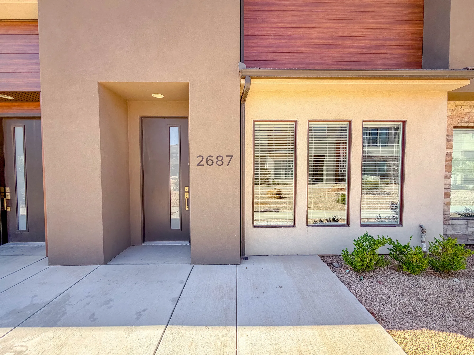 Modern architectural entry showcasing a clean-lined facade with a recessed entryway, horizontal wood-finish soffit detailing, and triple-pane sliding glass doors