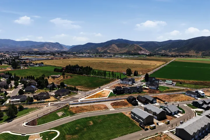 Expansive undeveloped lot featuring clear boundaries, surrounded by established residential properties and cultivated fields, with distant mountains defining the horizon