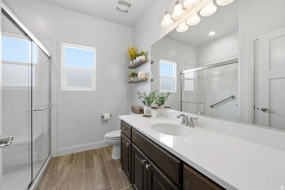 Bathroom featuring a dual-sink vanity with white countertop, wood-finish flooring, a glass-enclosed shower with bench, and two windows
