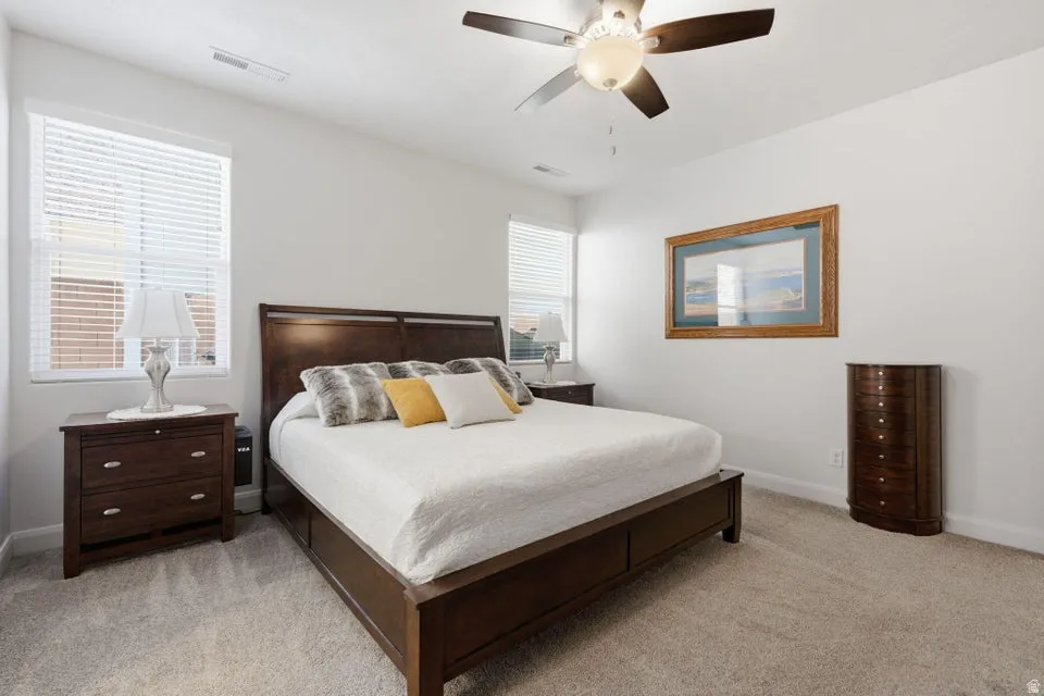 White-painted walls with two windows featuring blinds, neutral carpeting, and a ceiling fan with integrated lighting