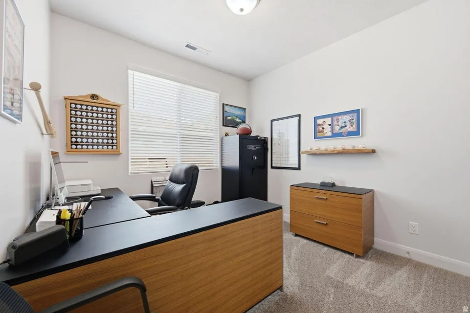 Professional office featuring a wood-finish desk with integrated work surface, ergonomic black task chair, and ample natural light from a large window with plantation shutters