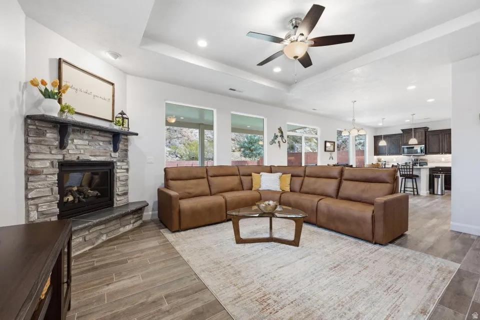 Stone-clad fireplace with hearth, wood-finish flooring, recessed lighting, and a ceiling fan
