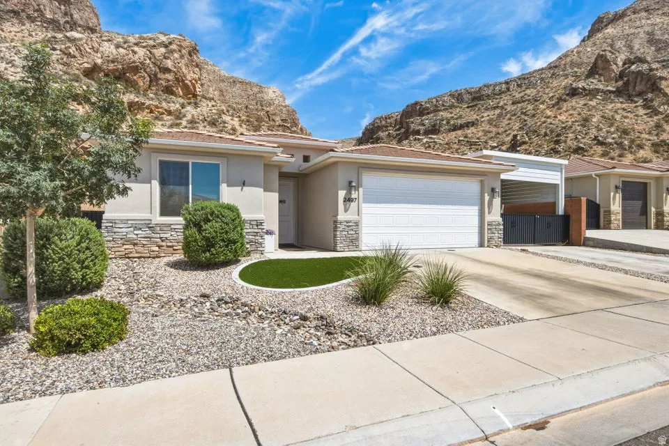 Exterior featuring a stucco finish with stone accents, a two-car garage, a concrete driveway, and an artificial turf landscape element
